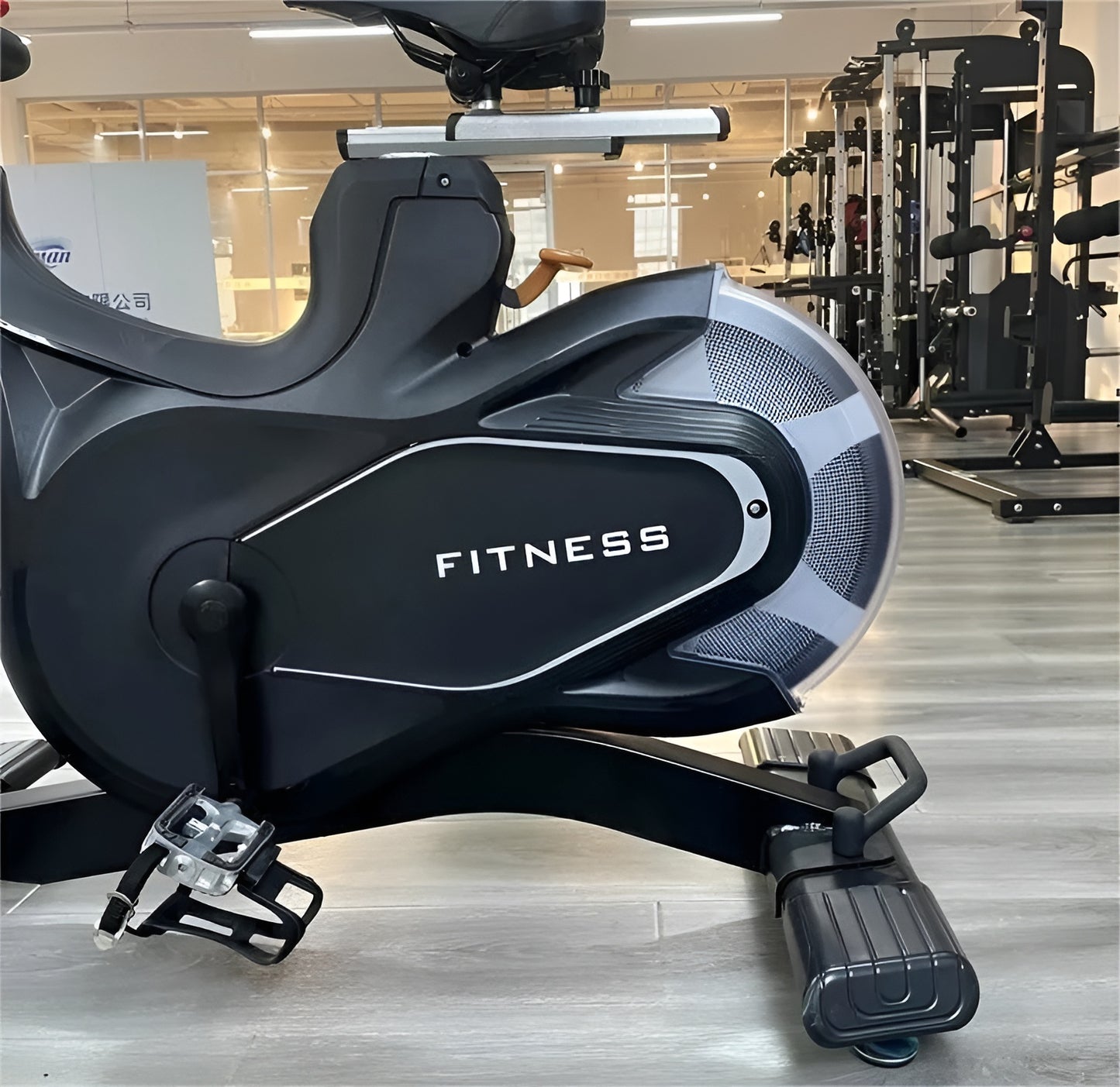 Vue rapprochée de la mécanique du vélo S3, montrant le carter marqué « FITNESS », la pédale avec cale-pied et la base avec roues de transport.