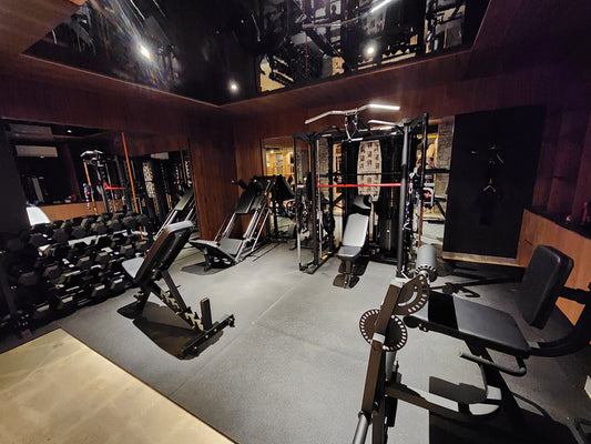 Salle d'entraînement haut de gamme conçue et aménagée par HALT3R Détaillant Fitness chez Concept M Rustique à Gatineau, incluant des équipements de musculation professionnels, des haltères et un banc ajustable sur un plancher en caoutchouc.