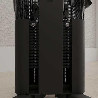 Vue détaillée des doubles piles de poids de 165 lb de la station d'entraînement Inspire FT1 PRO. Chaque pile est numérotée de 1 à 16, avec des plaques noires et une goupille de sélection chromée. Les colonnes sont protégées par des grillages métalliques. Mur de briques blanches en arrière-plan.