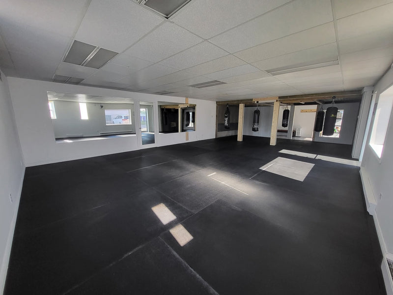 Aménagement intérieur d'un studio d'entraînement Puissance 2 Fitness avec dalles de sol sportives noires protectrices et sacs de frappe suspendus.