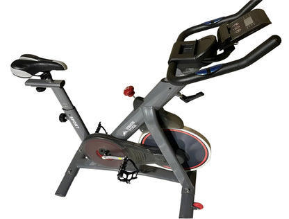 Vue en perspective trois quarts avant droite du vélo d'intérieur S1 gris de Summum Fitness, sur fond blanc. La selle, le guidon multi-positions avec la console et le pédalier avec cage sont visibles.