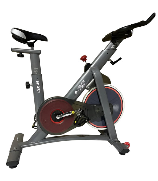 Vue de profil droite du vélo d'intérieur S1 gris de Summum Fitness, sur fond blanc. On distingue clairement la structure du cadre, le volant d'inertie avec le logo et le mécanisme de résistance.