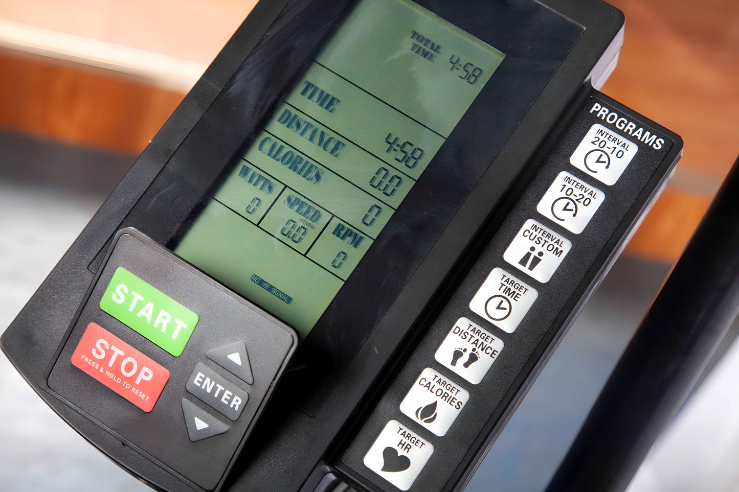 Gros plan détaillé de la console numérique et du panneau de commande du vélo à air. L'écran LCD affiche les données d'entraînement (temps, distance, calories, watts, vitesse, RPM). Les boutons en caoutchouc verts et rouges sont clairement visibles ("START", "STOP"), ainsi que les touches de programme et de cible sur le côté droit.